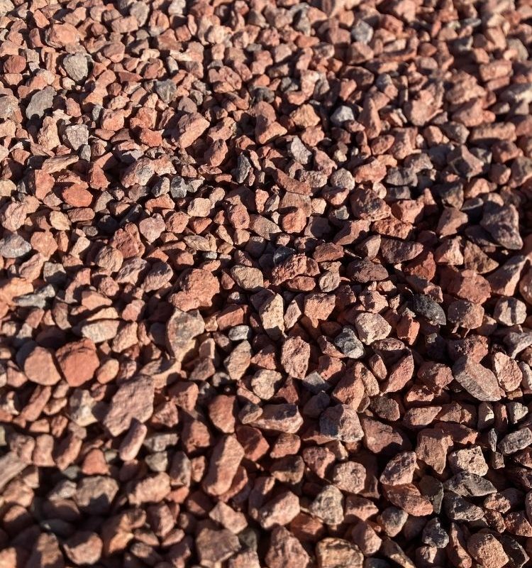 Close-up of red landscaping gravel ground cover, small crushed stones with sunlit textured background