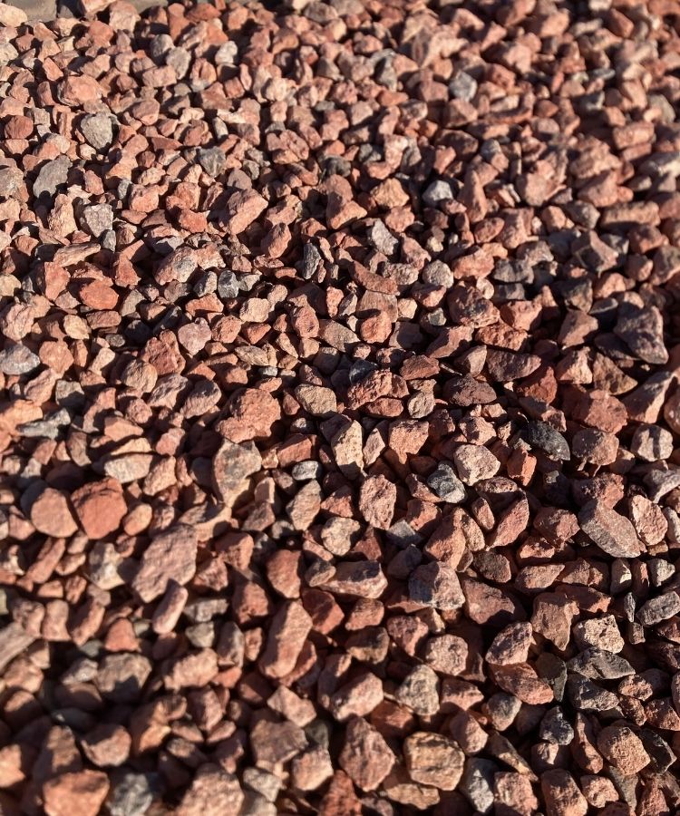 Close-up of red landscaping gravel ground cover, small crushed stones with sunlit textured background