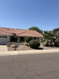 Single-story Southwest home with red tile roof, xeriscape front yard, palm tree and American flag under clear blue sky.