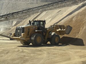 CAT wheel loader moving sand at quarry near conveyor belts, heavy equipment for mining and aggregate operations.