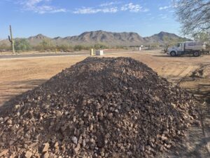 Desert construction site with gravel pile, water truck, and saguaro cactus against Arizona mountain landscape.