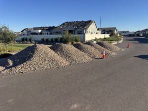 Piles of landscaping gravel with traffic cones on suburban street near new homes under construction.