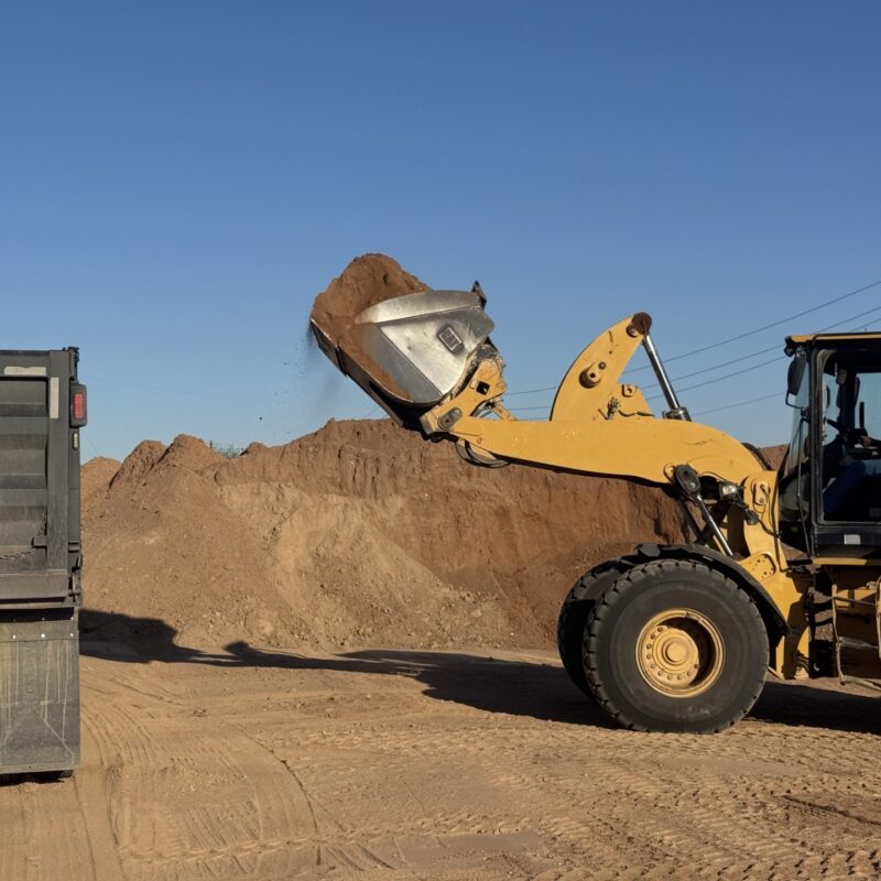 Wheel loader dumping dirt into dump truck at construction site, earthmoving and hauling soil under clear sky