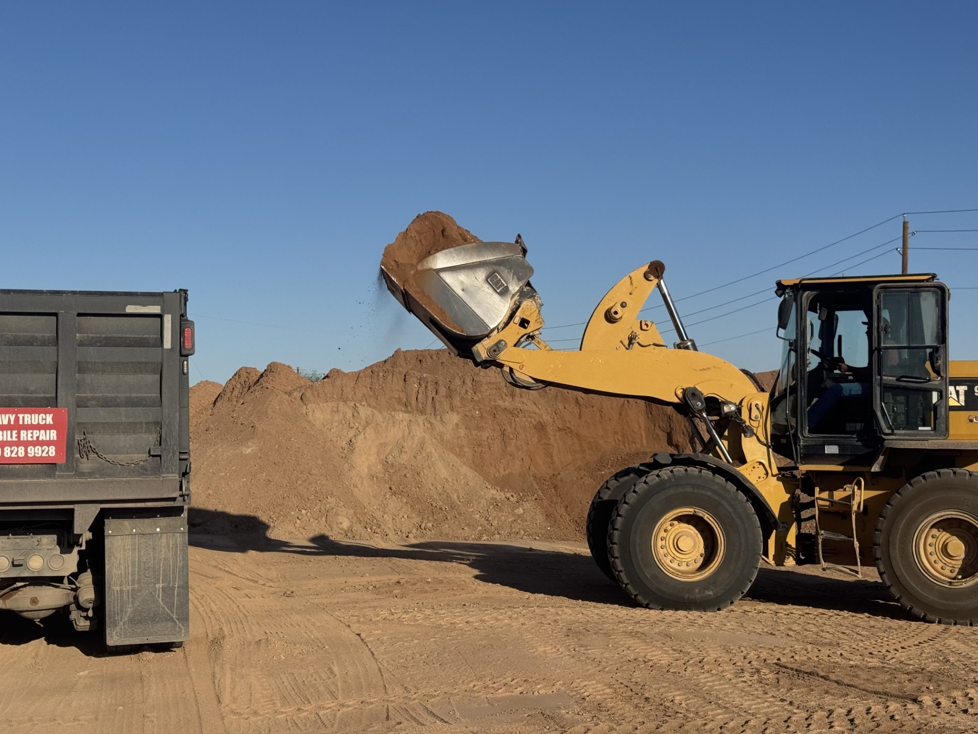 Wheel loader dumping dirt into dump truck at construction site, earthmoving and hauling soil under clear sky