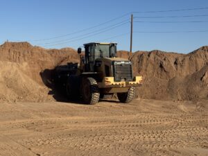 CAT wheel loader scooping dirt at construction site, heavy equipment moving soil by sand piles under blue sky
