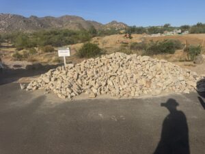 Granite rock pile at desert construction site with Available sign and mountains in background