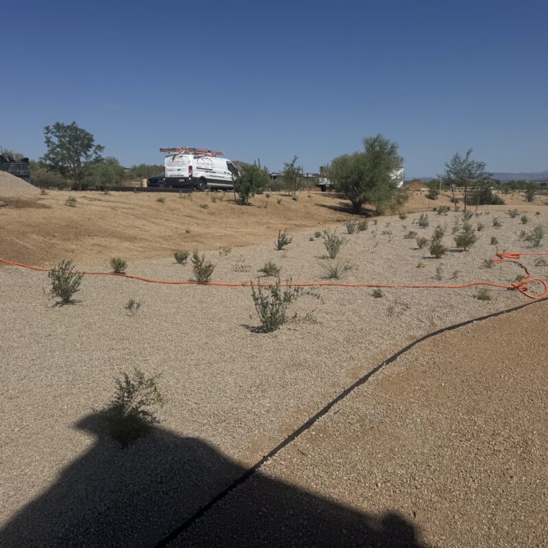 Desert landscaping project: gravel xeriscape with native shrubs and orange drip irrigation lines, work van in background.