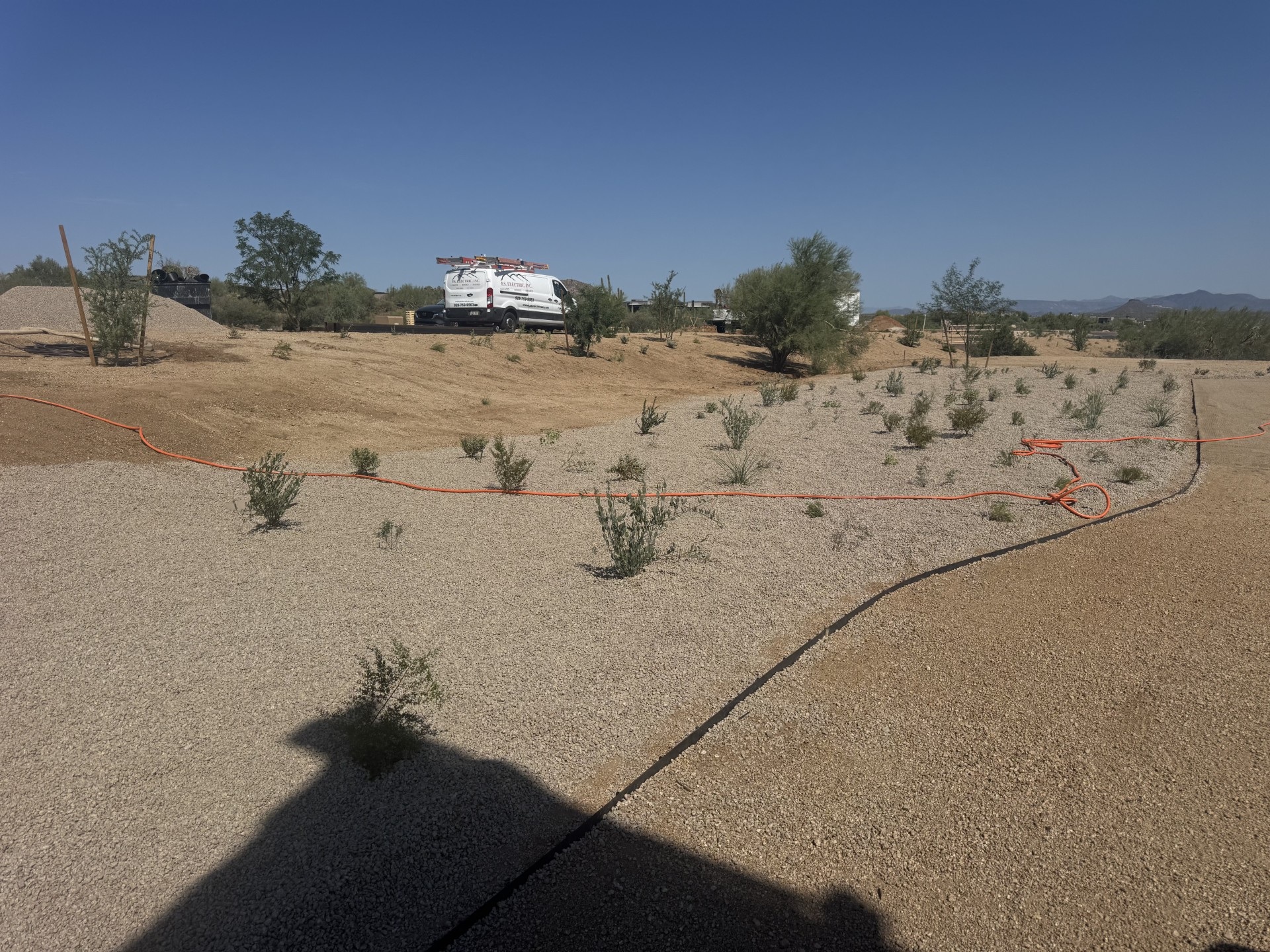Desert landscaping project: gravel xeriscape with native shrubs and orange drip irrigation lines, work van in background.