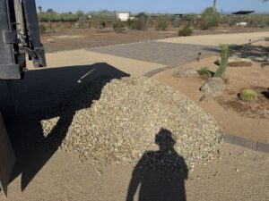 Fresh gravel pile delivered on desert landscaping driveway with cacti, rocks, and pavers in xeriscape yard